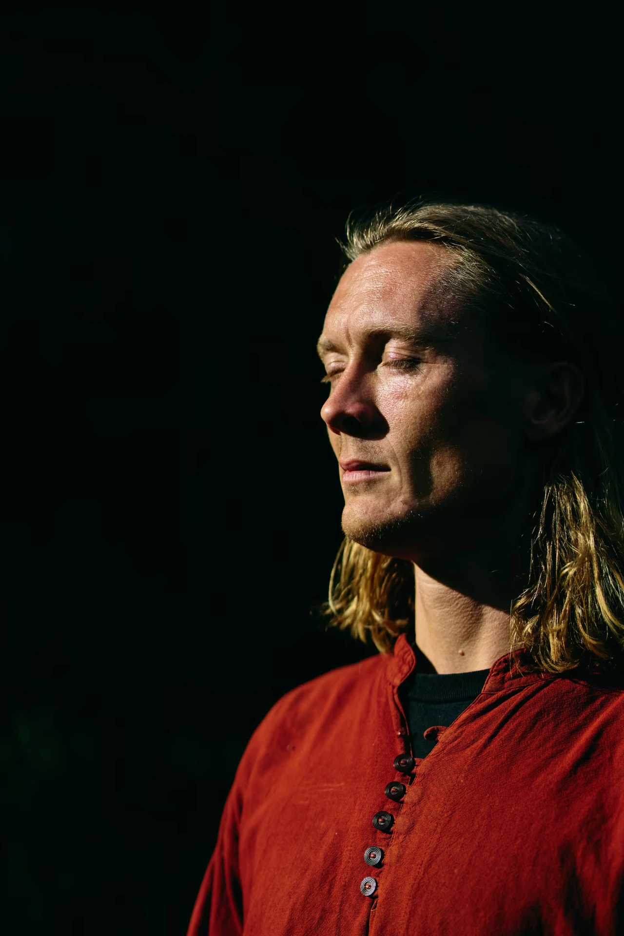 Portræt af Simon Skipper med lukkede øjne i skarpt sidelys mod mørk baggrund.