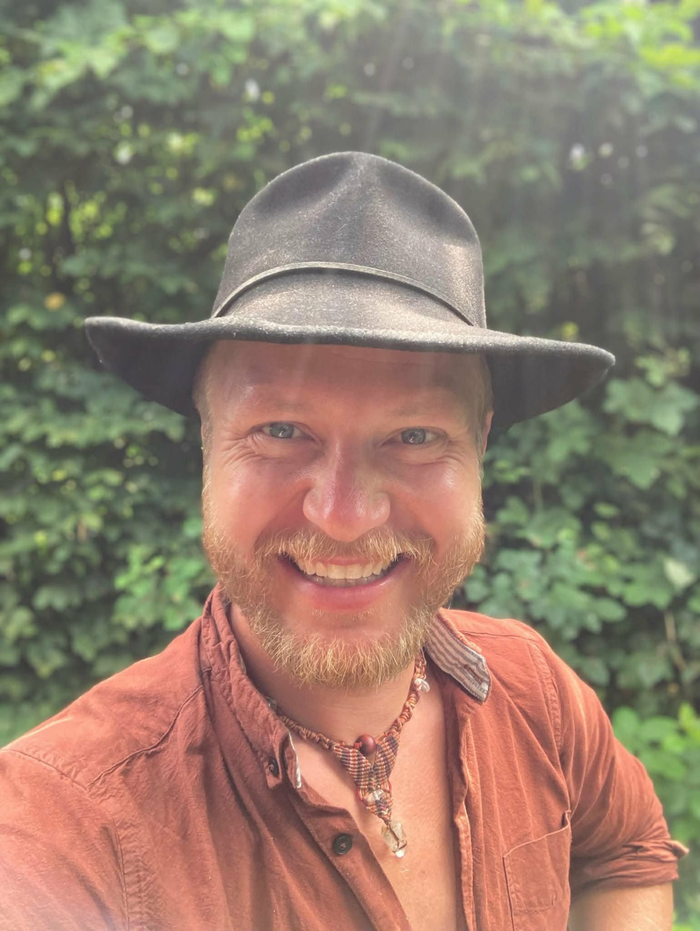 Portræt af Mads Harboe med hat foran grønne blade.